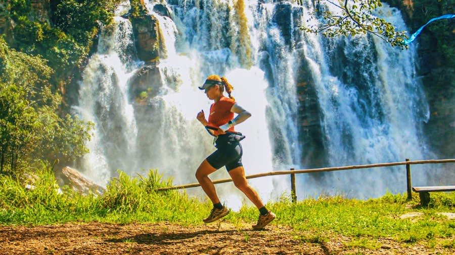 Corredora passando em frente a uma cachoeira larga durante um treino em trilha